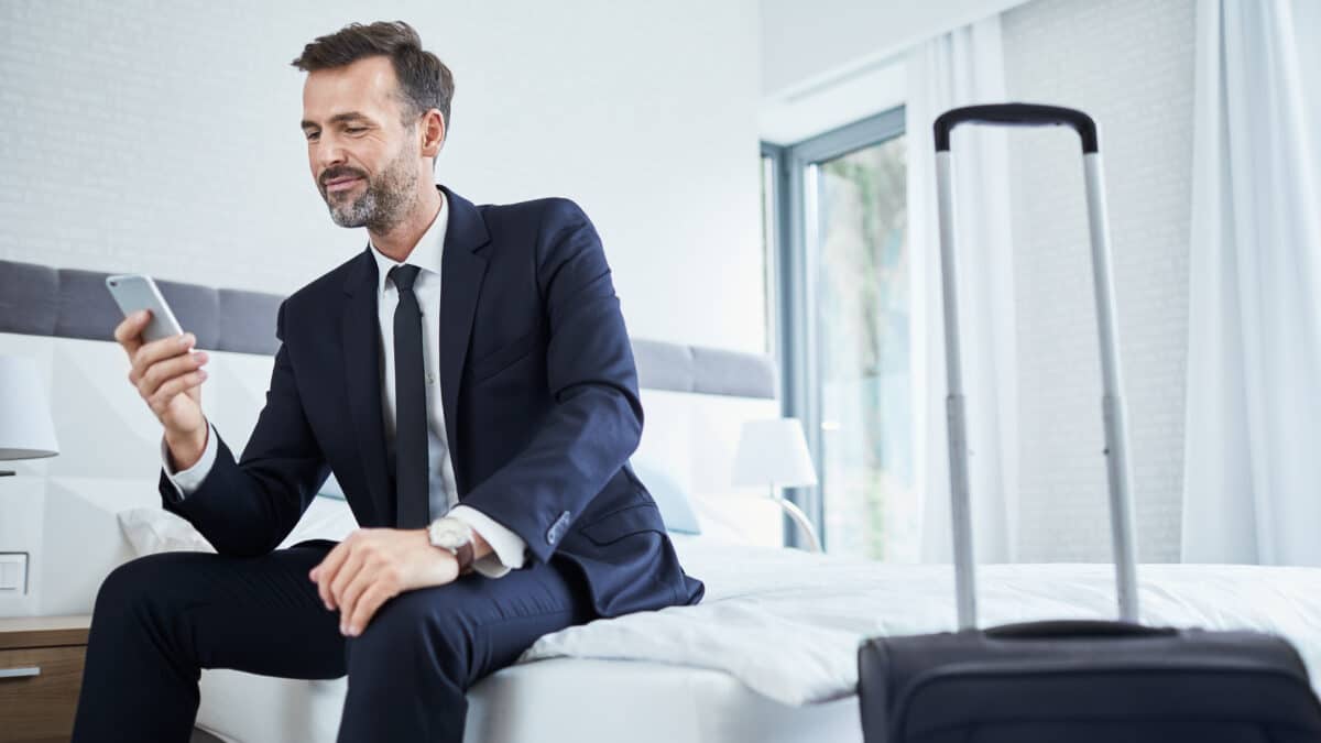 Business man in a suit uses a mobile phone in his hotel, emphasizing mobile security during travel.