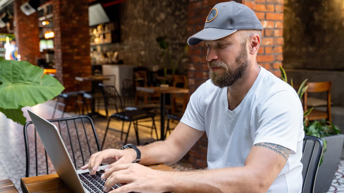 Man in casual clothes uses laptop in cafe, highlighting significance of cybersecurity in remote work