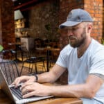 Man in casual clothes uses laptop in cafe, highlighting significance of cybersecurity in remote work