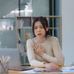 Stressed employee at desk sees malware icons on her laptop screen, representing a malware attack.