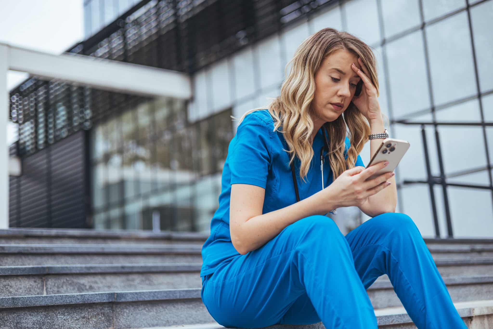 A tired physician sits outside a hospital, symbolizes how AI scribes can reduce healthcare fatigue.