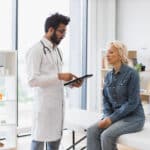 Doctor explains his use of an AI scribe to elderly patient while using his tablet in the exam room.