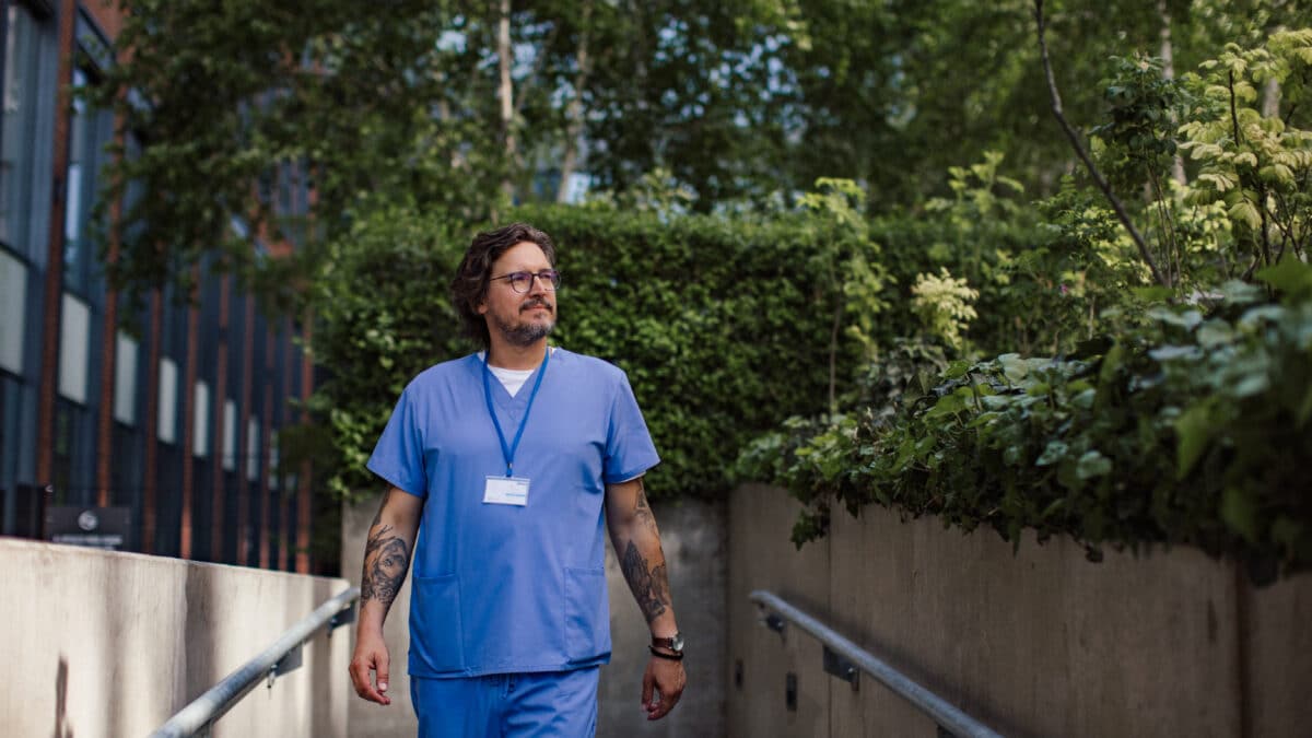 Doctor in scrubs walking outdoors, illustrating improved work-life balance with AI scribes.