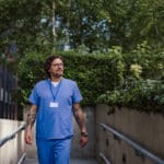 Doctor in scrubs walking outdoors, illustrating improved work-life balance with AI scribes.