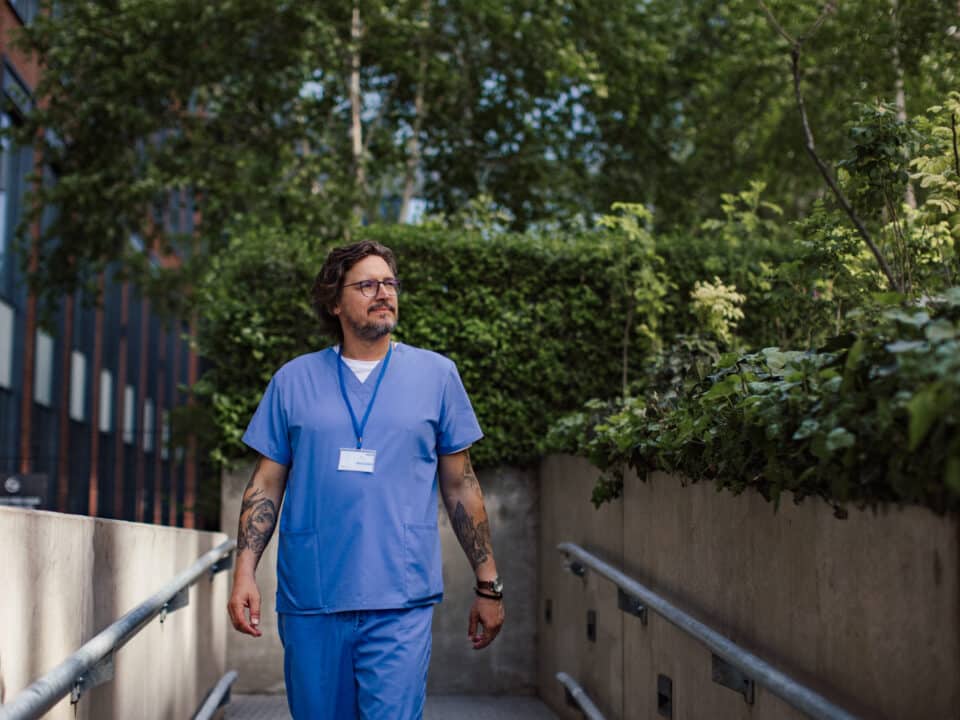 Doctor in scrubs walking outdoors, illustrating improved work-life balance with AI scribes.