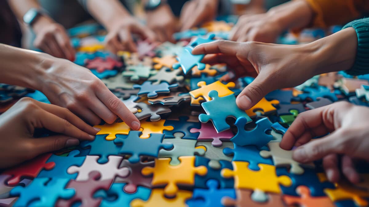 Hands collaboratively assemble colorful puzzle pieces; symbolizes teamwork in AI scribe integration.