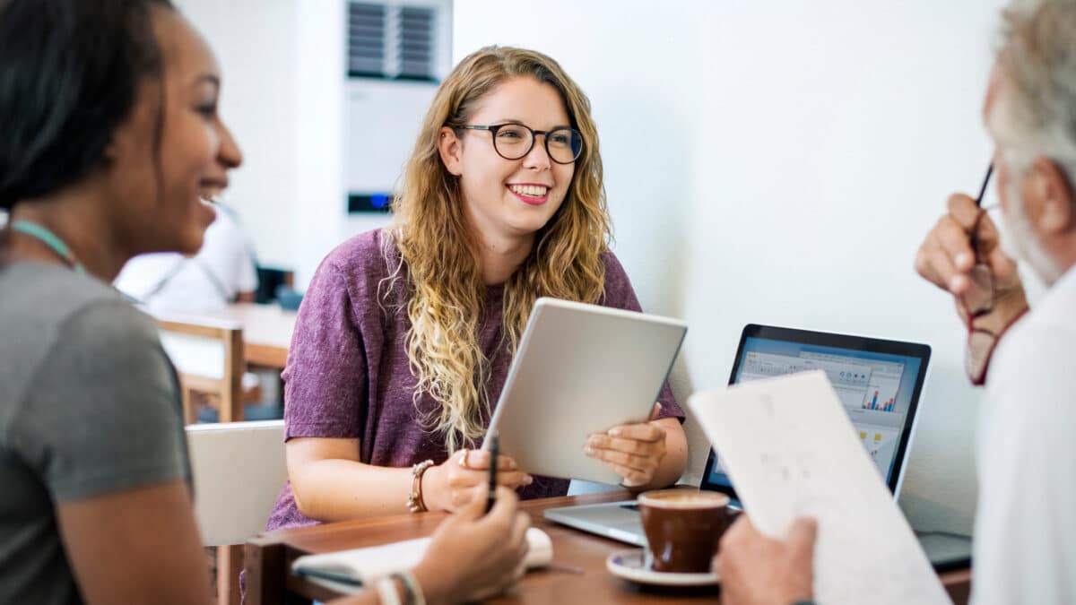 Happy colleagues use AxiScribe AI for efficient meeting note-taking with digital devices.