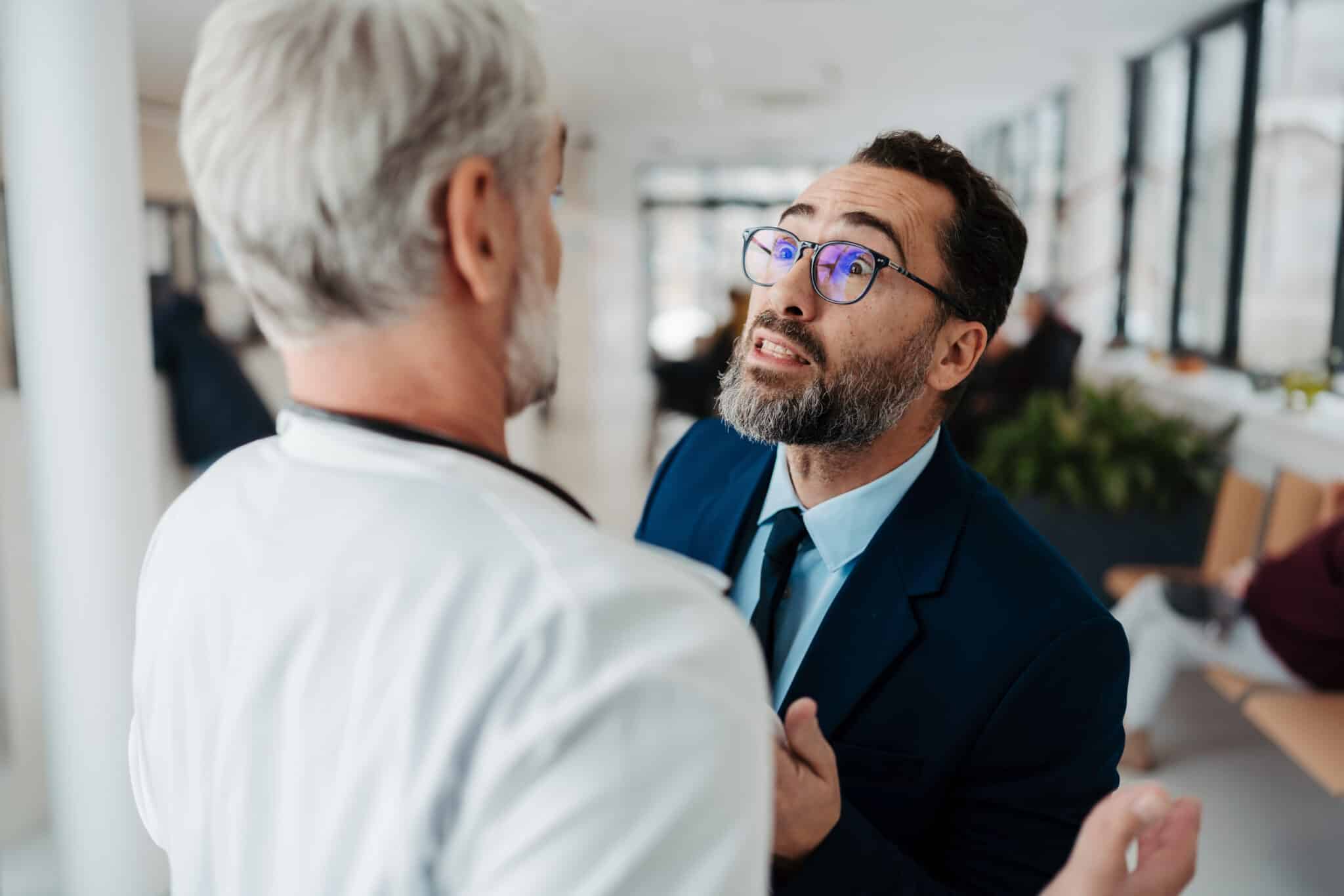 Man in suit urgently speaks with doctor, highlighting stress and need for AI scribes in healthcare.