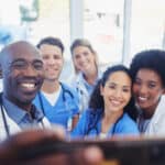 Healthcare, team and selfie by doctors at hospital, happy and proud , smile and bond on blurred background. Medical, diversity and group pose for photo, profile picture or website homepage update.