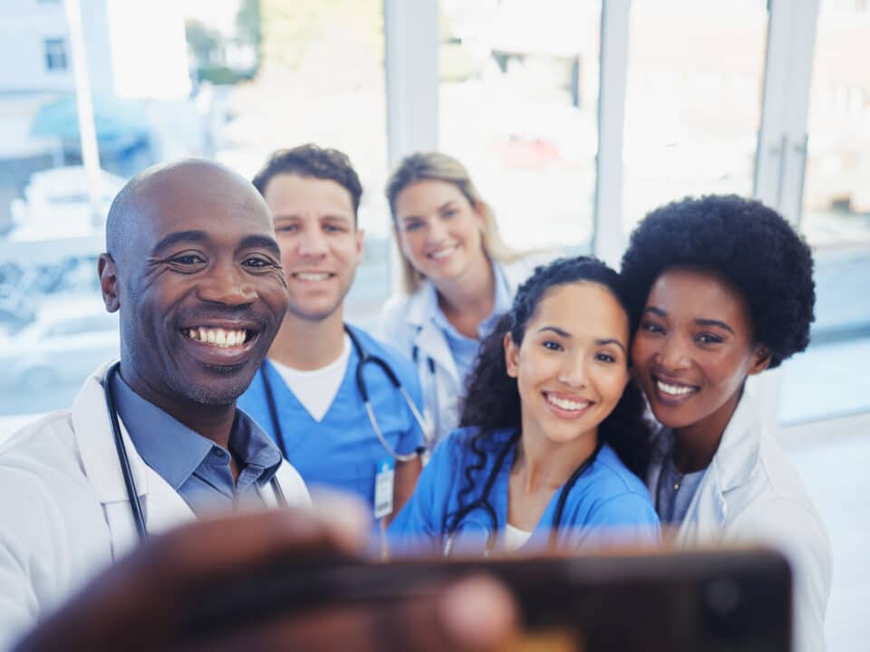 Healthcare, team and selfie by doctors at hospital, happy and proud , smile and bond on blurred background. Medical, diversity and group pose for photo, profile picture or website homepage update.