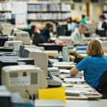 Government transcription office with staff working at desks filled with computers and files.